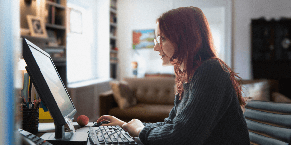 Woman with red hair, glasses, and a long sleeve sweater using a desktop computer in her office